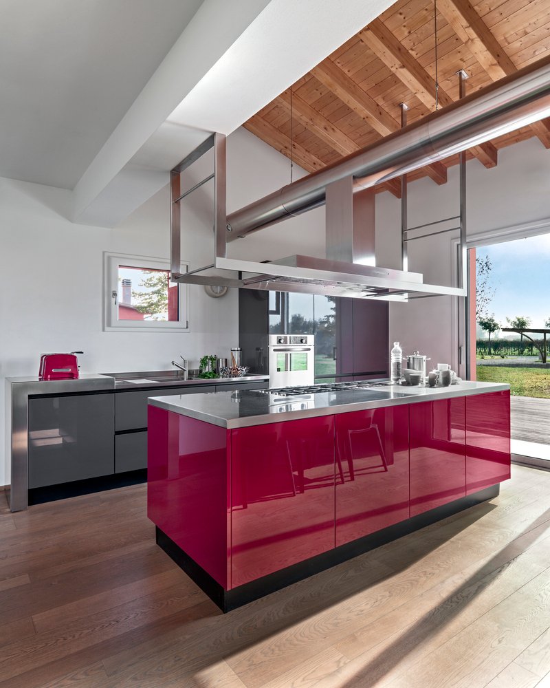 interiors of a modern red lacquered kitchen in the foreground the island kitchen, the floor is in wood and the ceiling is in exposed wooden beams