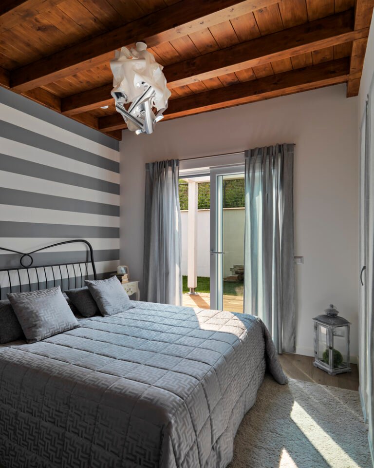interiors shots oh a modern bedroom with wooden ceiling , modern chandelier and stiped wall